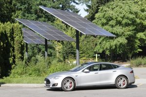 An image of one of many solar-powered cars parked near solar panels.